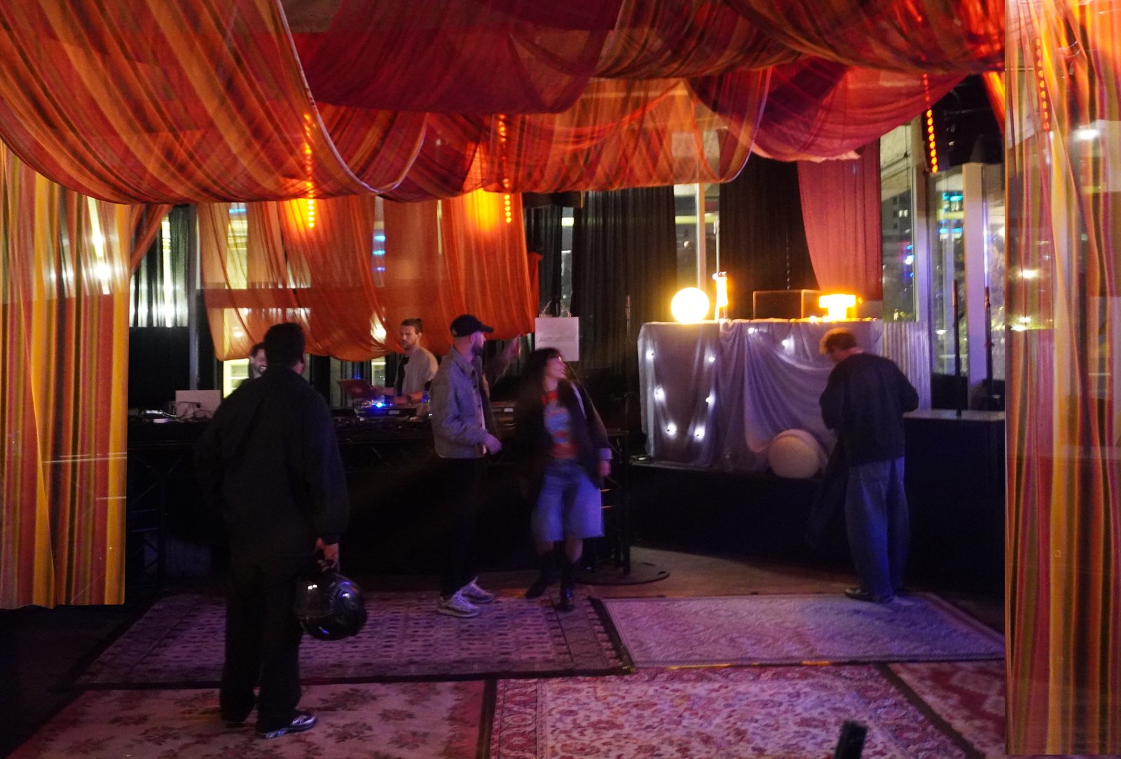 The LAB room dressed in draped orange and red fabrics, with a lamp-lit DJ booth and patterned rugs, guests arriving