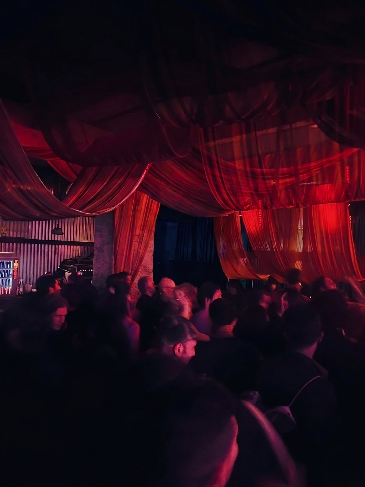 Dense crowd in red light under the draped ceiling
