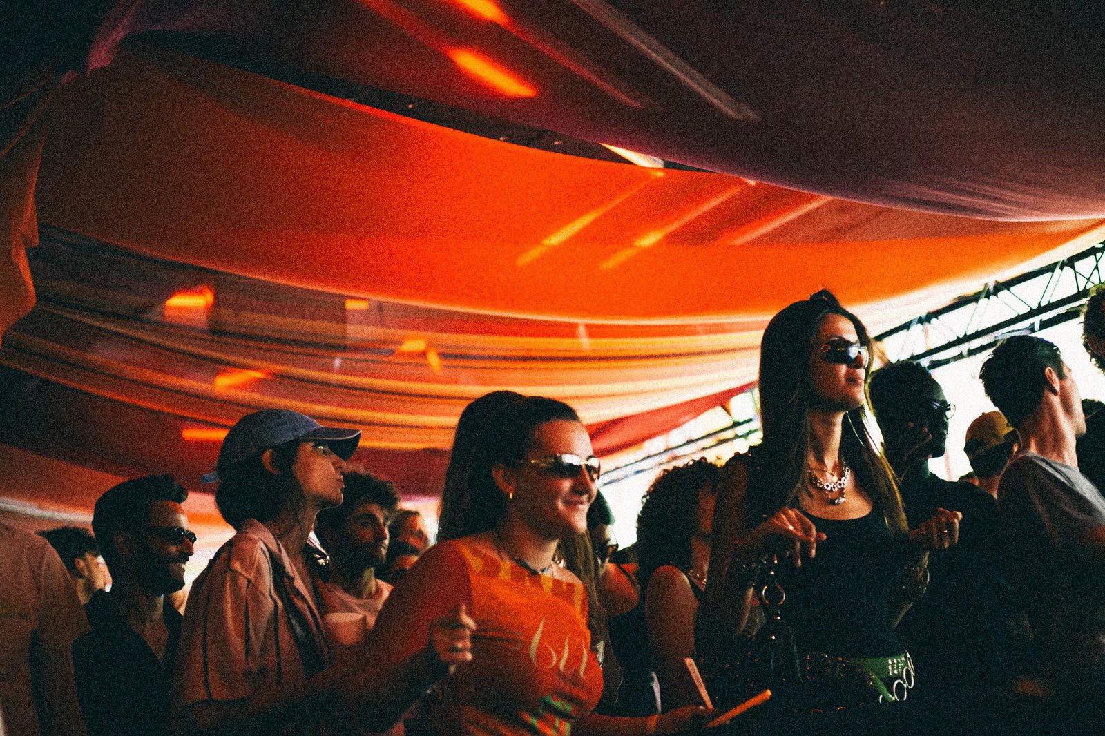 The crowd dancing under a canopy of orange-lit drapes, lit rings glowing above the booth