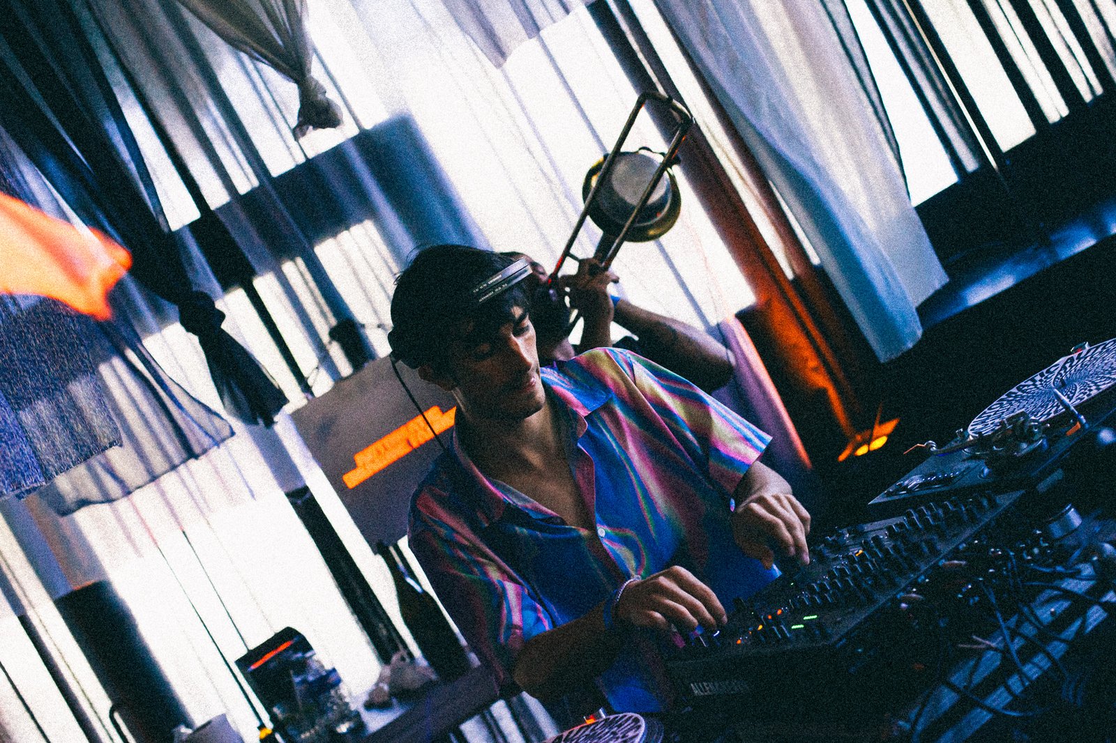 A DJ in a purple shirt playing amid the blue drapes, a brass light fitting overhead