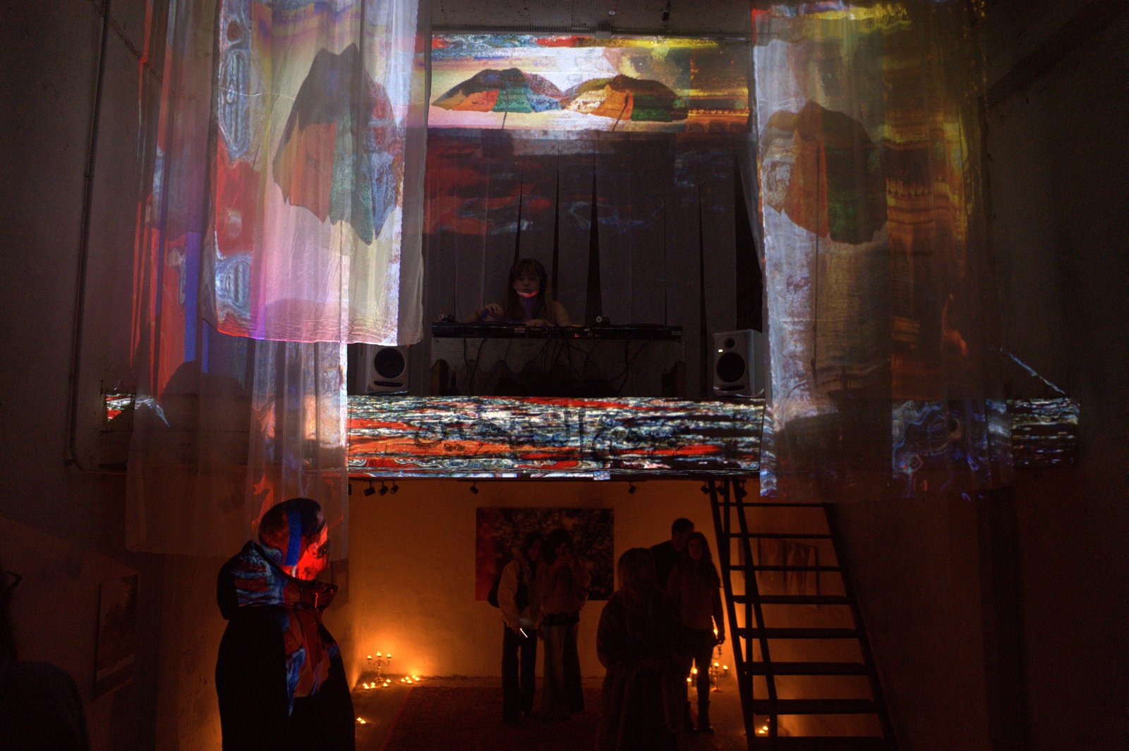 Inside the venue: sheer fabrics hung from the mezzanine carry moving projections while the DJ plays above and guests stand below by a metal staircase