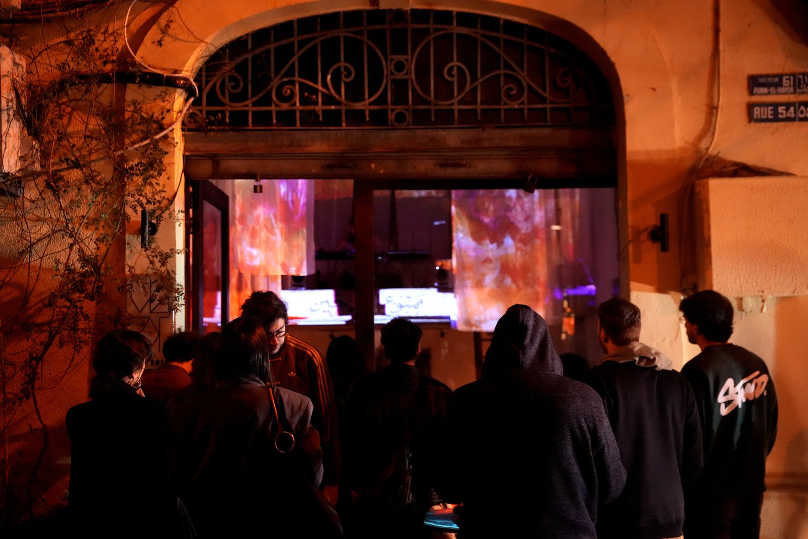 Outside the venue at night: a crowd looks through the arched doorway at the projections glowing inside
