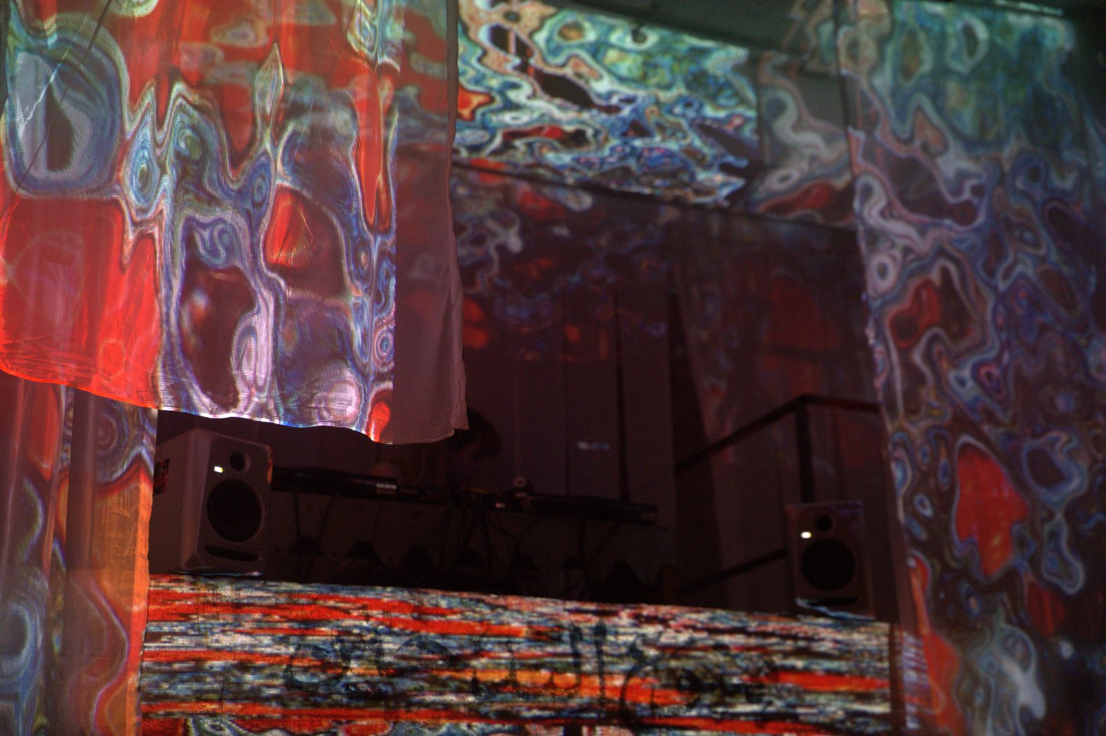Close view of the projected fabrics: swirling red, blue and white patterns over the speakers and mixing desk