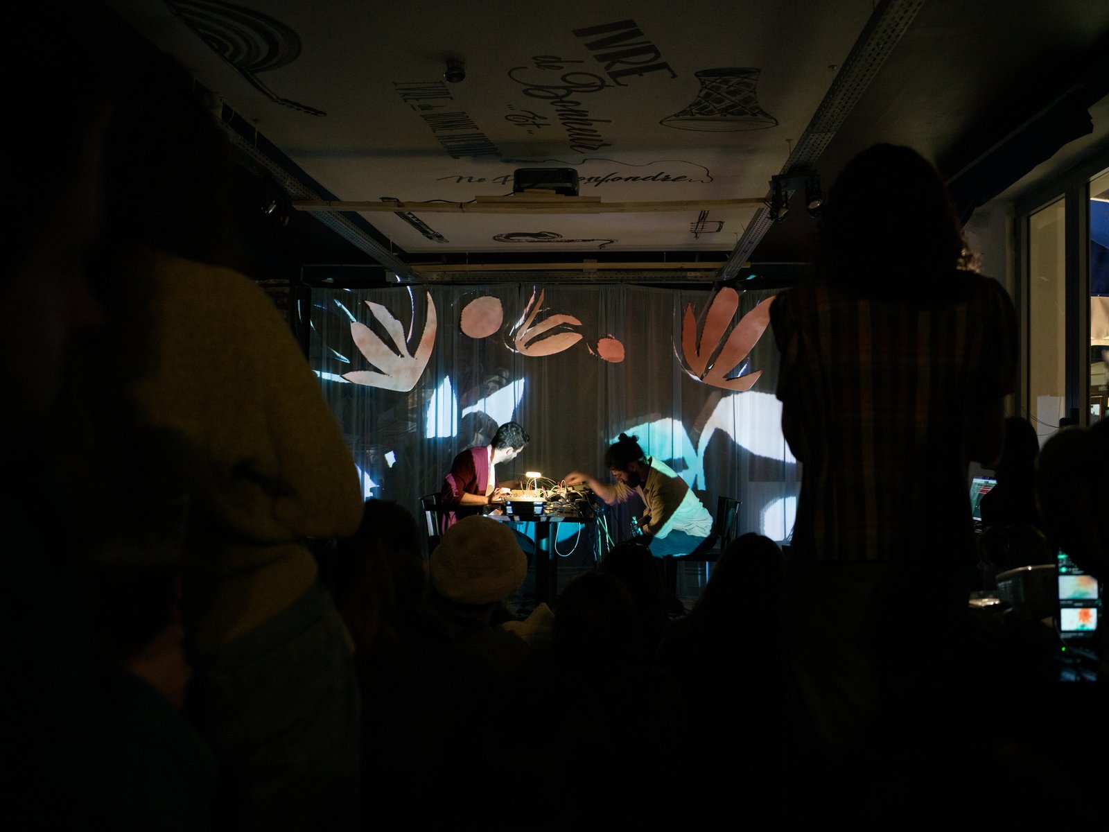 The audience in the dark looking towards the lit stage and projected shapes