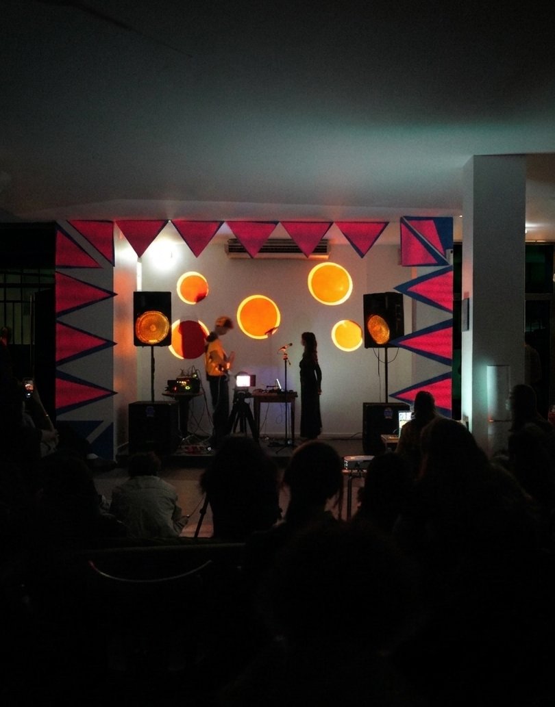 Portrait view of the stage: orange glowing discs and pink zigzag banners frame the performers