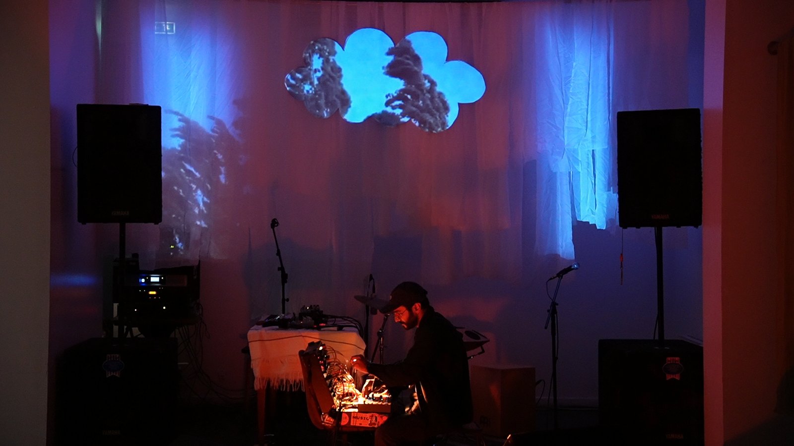 The cloud screen glowing blue above a seated performer, projections on the wall behind
