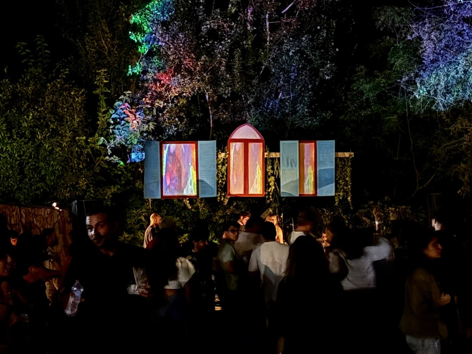 The crowd at night in front of the glowing shutters, the trees lit blue and pink