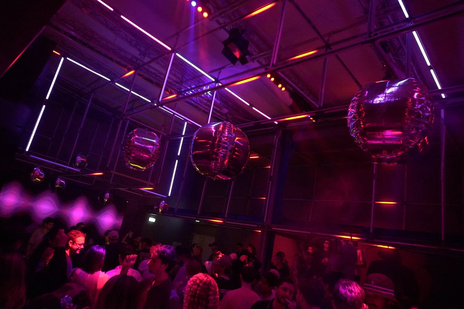 A scaffold cube hung with white light tubes and mirror balls above the dance floor, bathed in magenta