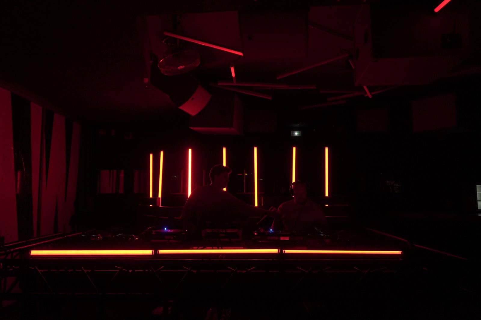 The CLUB room in deep red with vertical orange light bars behind the DJs